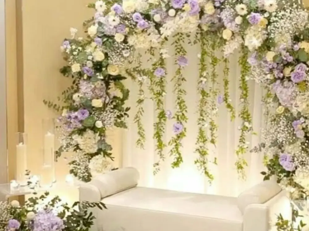 Pastel roka setup with a lavender and ivory floral arch, hanging greens and a cream sofa