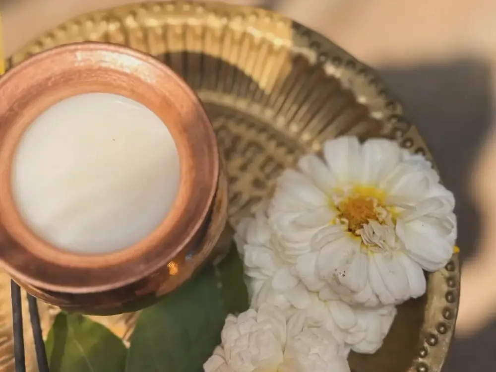 Copper pot of milk with white chrysanthemums on a brass thali