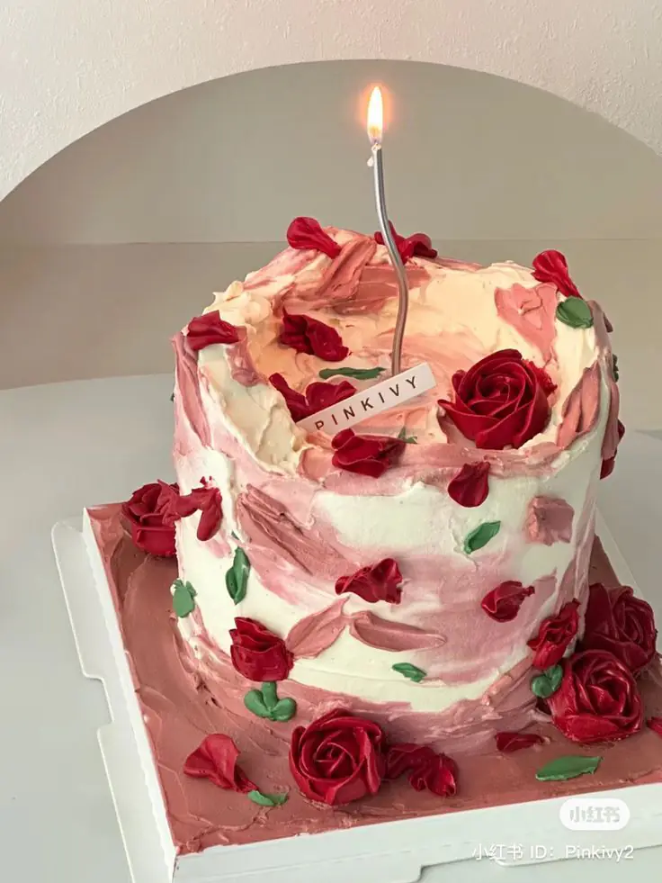 A frosted birthday cake decorated with red roses and a lit candle