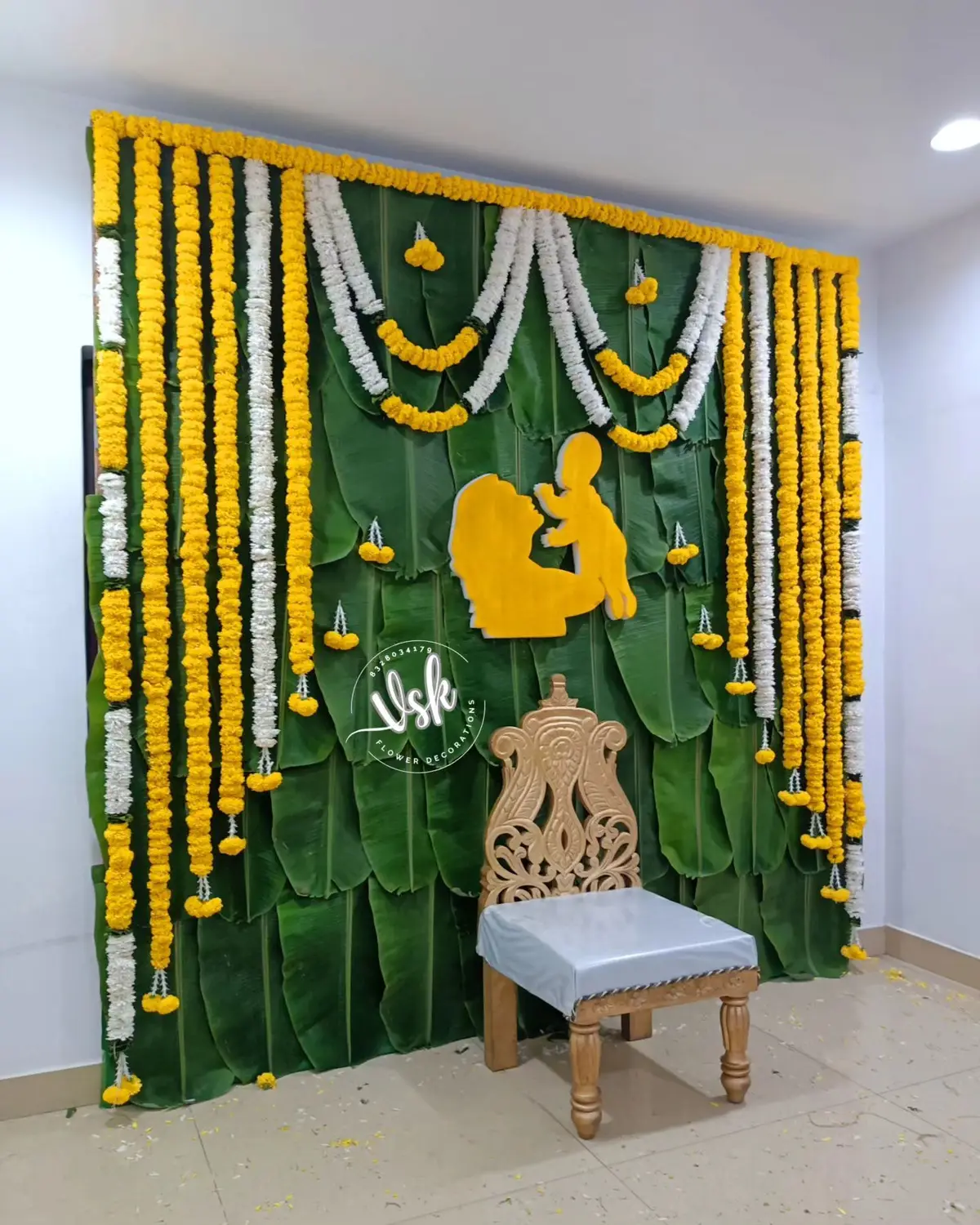A godh bharai backdrop of banana leaves and marigold strings with a carved wooden chair