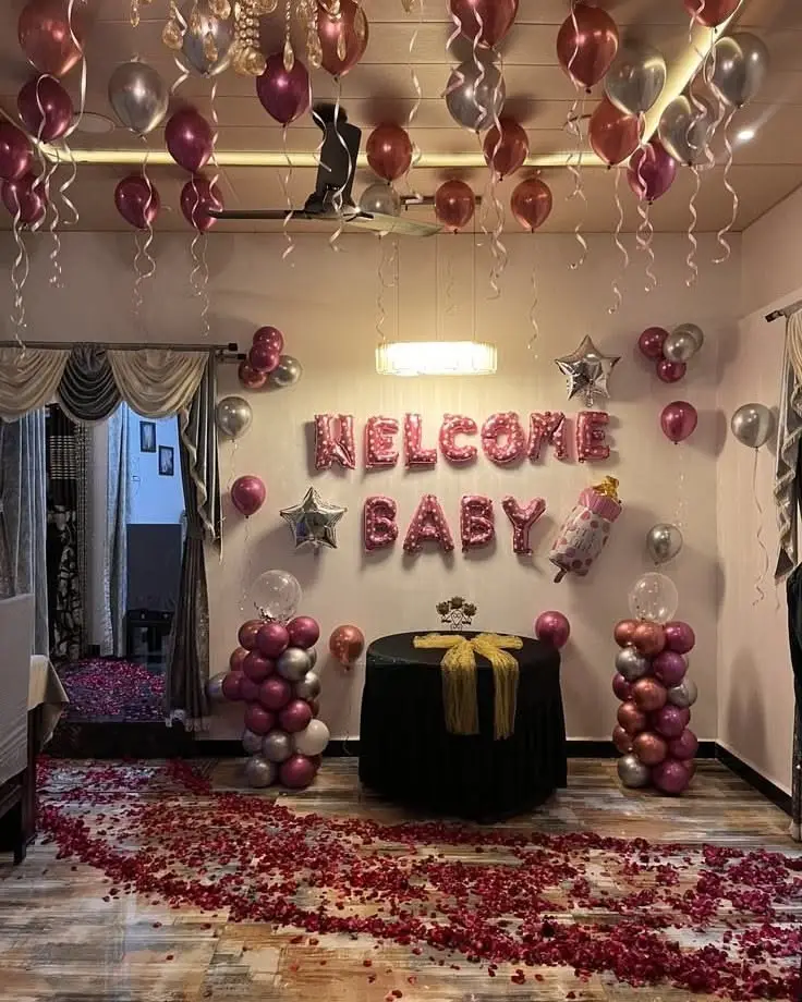 A room with Welcome Baby foil letters, pink balloons and a rose petal path
