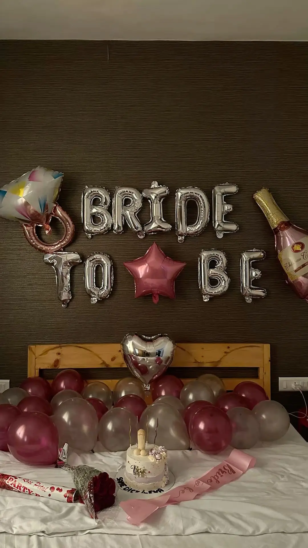 A bed with Bride To Be foil letters above and red and silver balloons around it