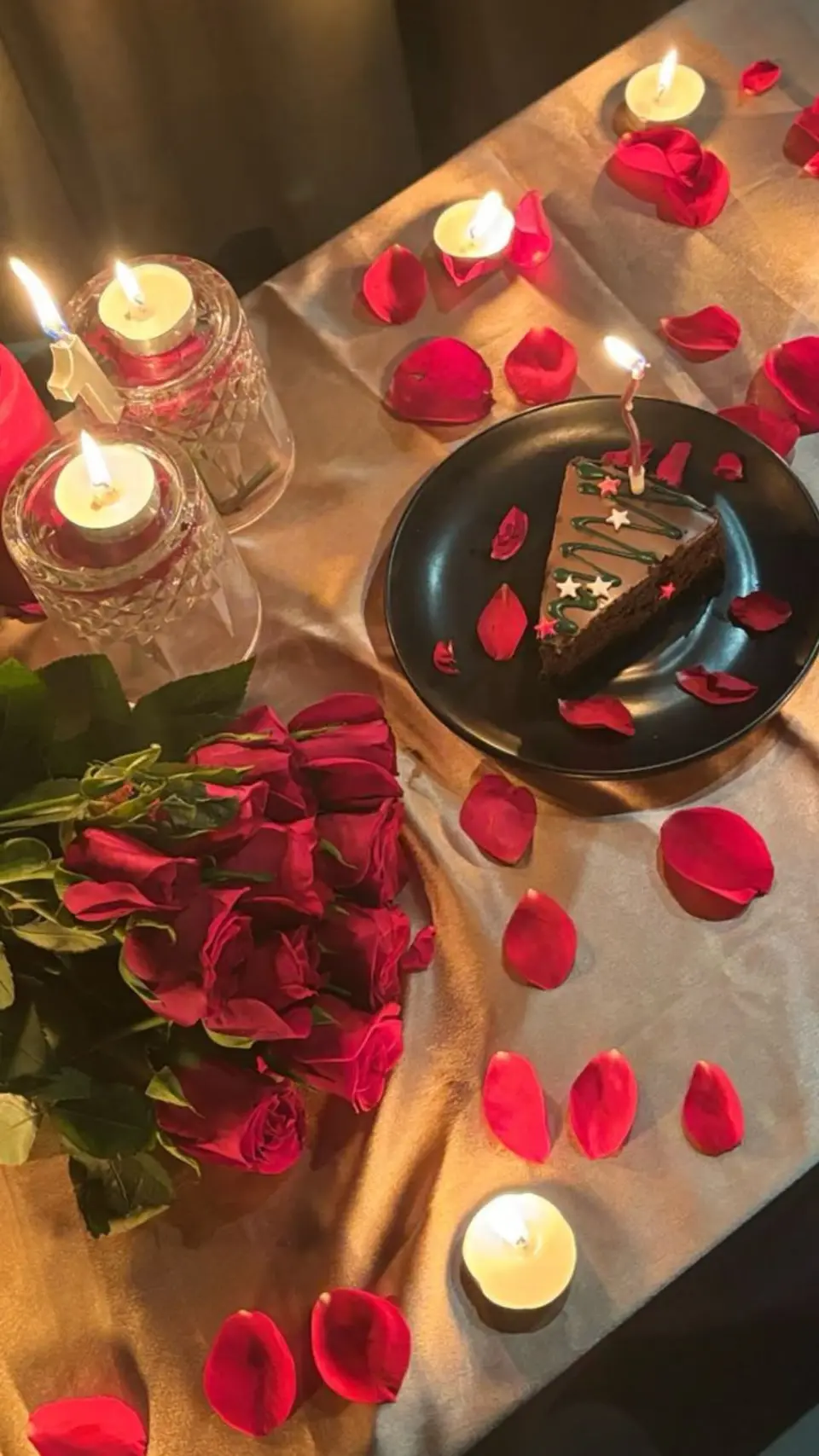 A table with rose petals, a bouquet and candles seen from above