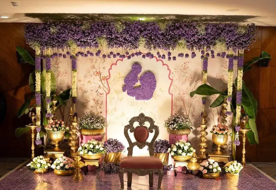 A stage backdrop of purple flowers with brass lamps and a chair