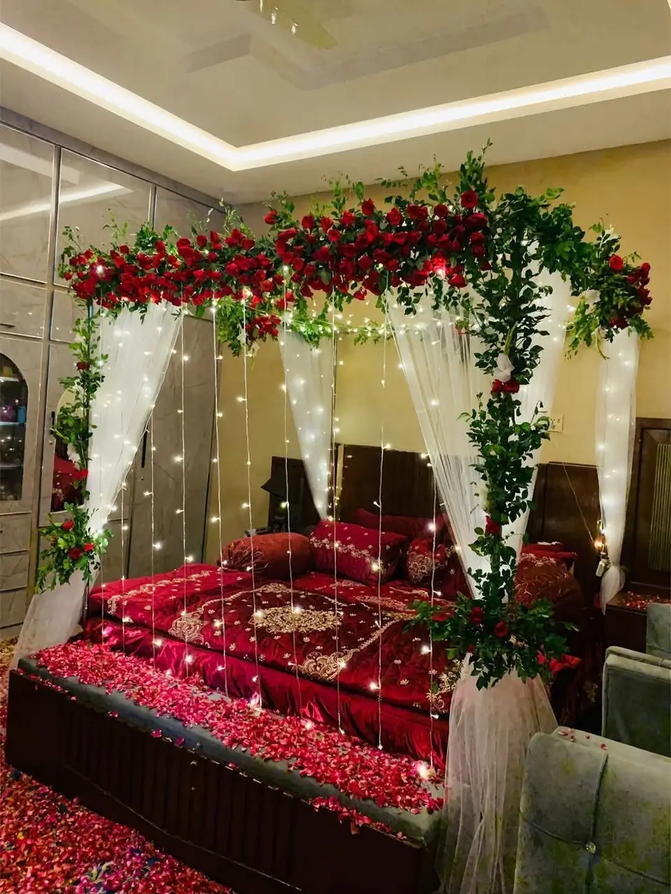 A hotel bed under a flower-topped canopy with red petals