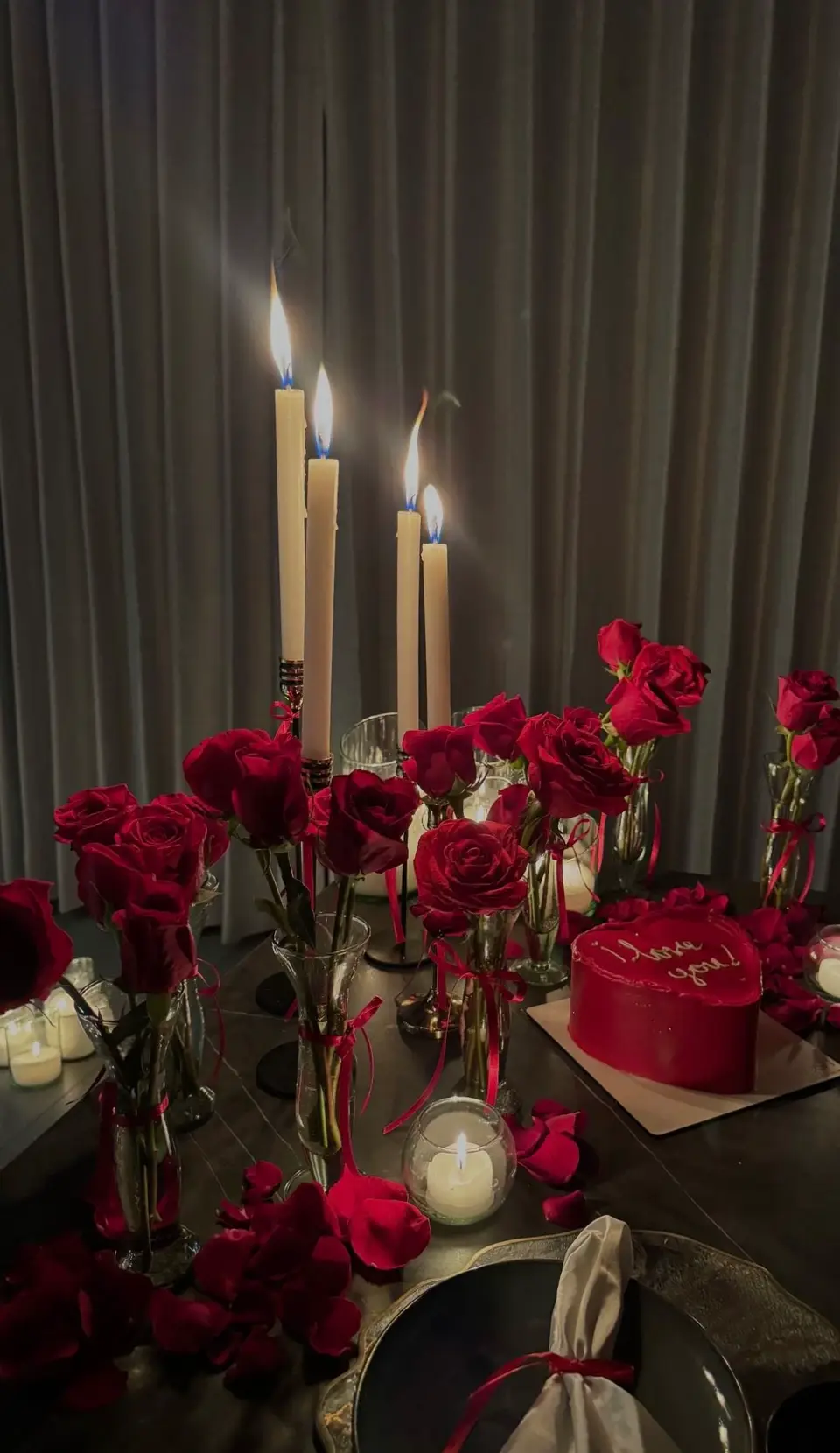 A candlelit table with tall candles and red roses around the plates