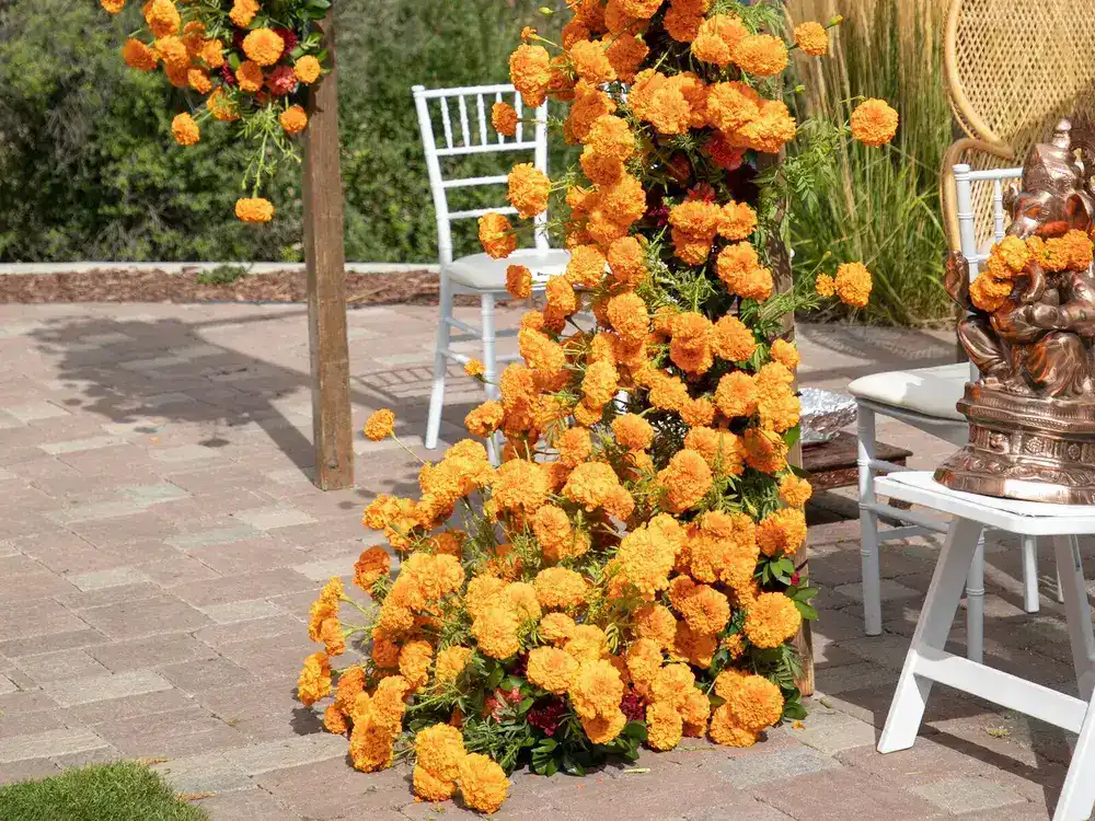 Wooden mandap frame with orange marigolds cascading down one post, a white chair and a copper Ganesh idol beside it