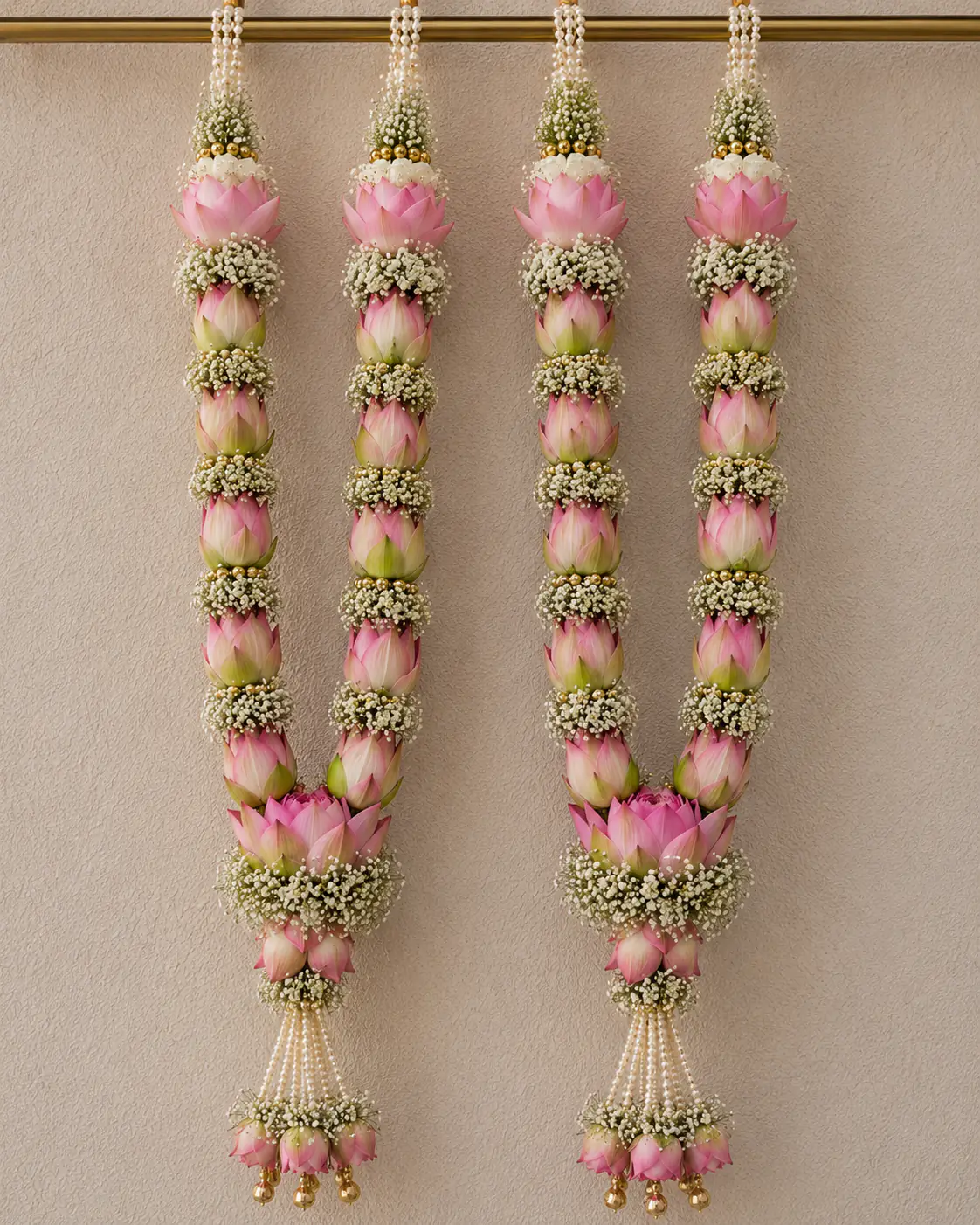 Pair of varmalas with pink lotus buds and jasmine hanging against a plain wall